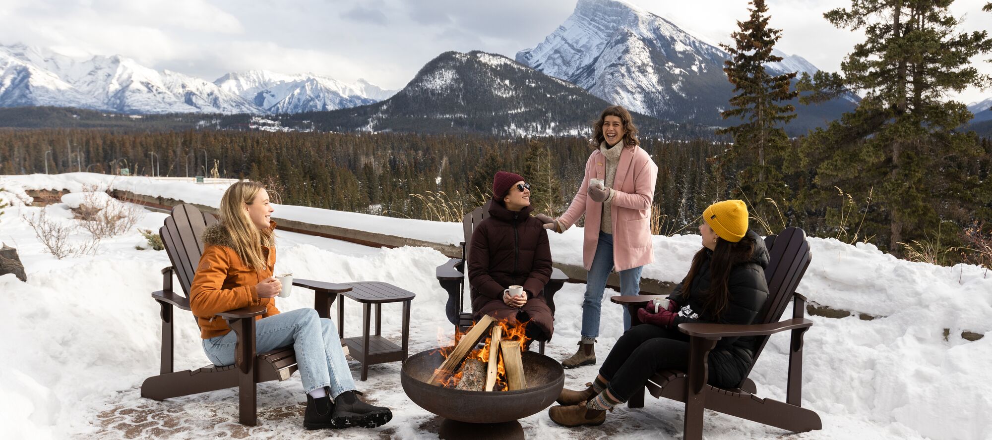 Friends enjoy hot chocolate on the patio of the Juniper Bistro in Banff National Park during winter.